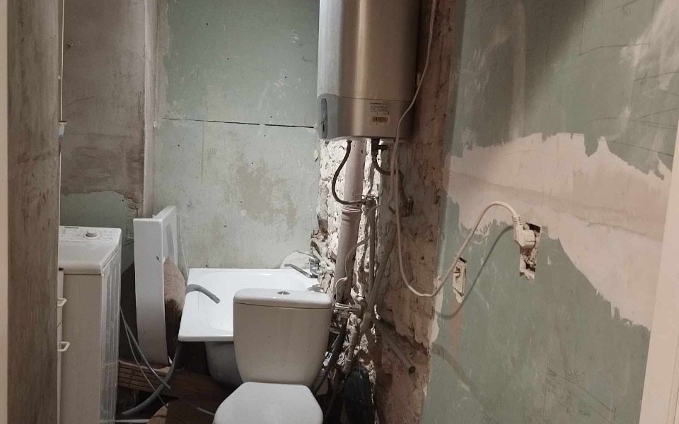
        Zniszczona łazienka z widocznymi instalacjami.
    