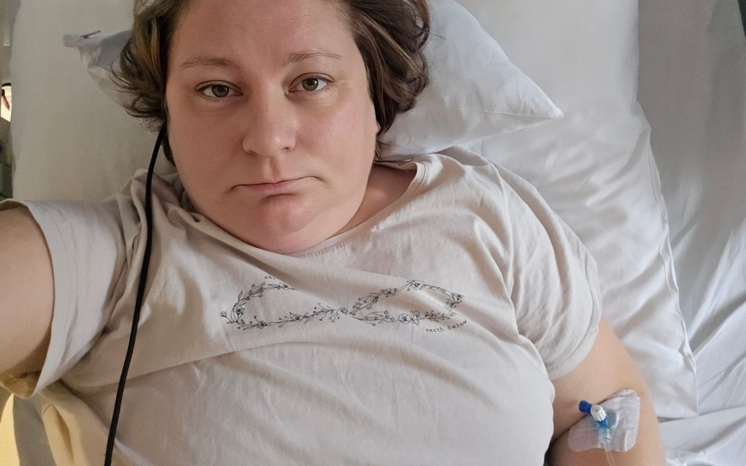 Kobieta leżąca w łóżku szpitalnym, z kroplówką i smutnym wyrazem twarzy.