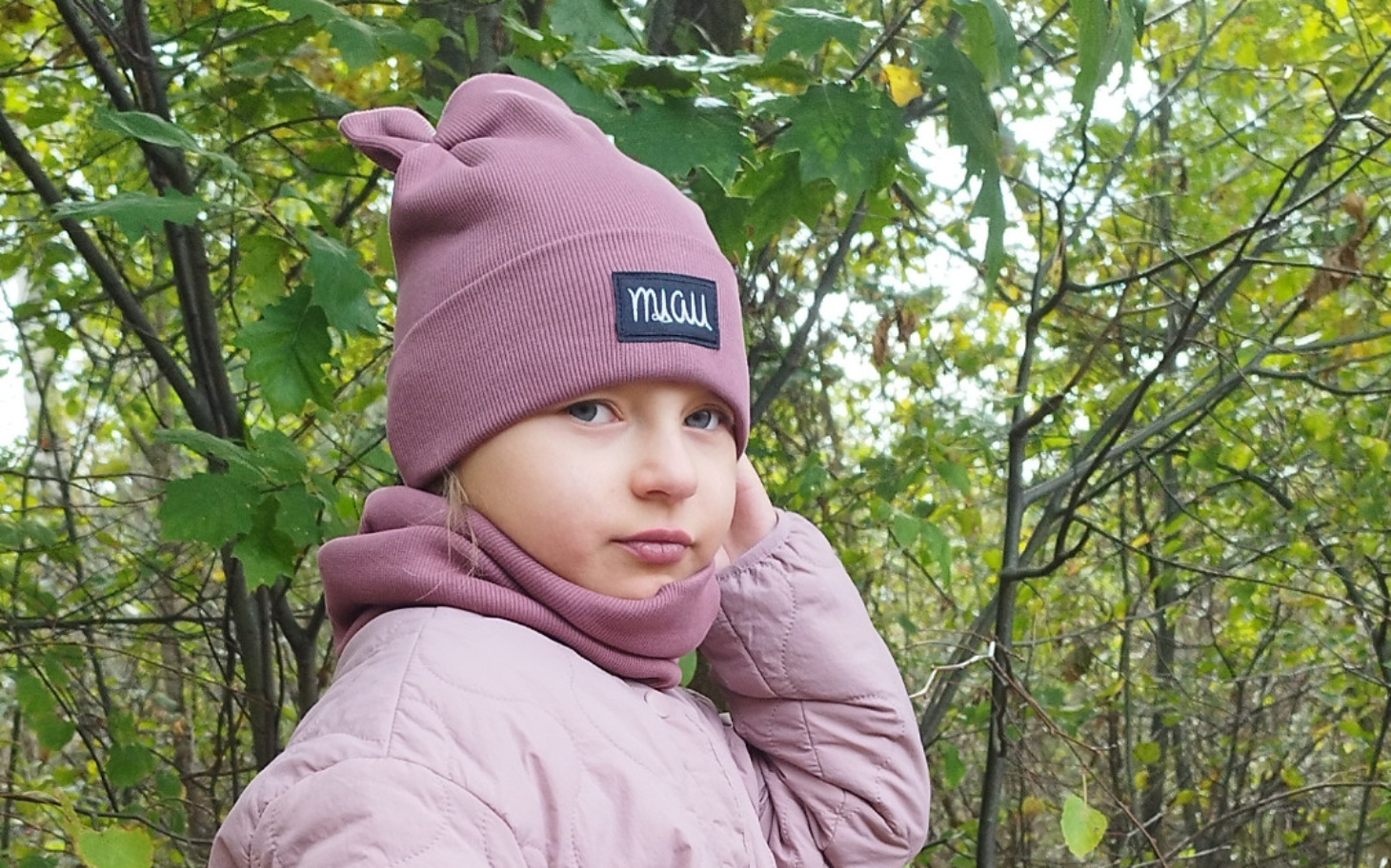 
        Dziewczynka w lesie, ubrana w różową czapkę i szalik.
    