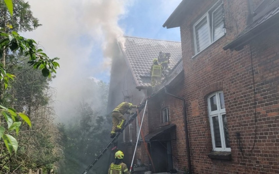 Strażacy gaszący pożar w budynku, dym unosi się w powietrzu.