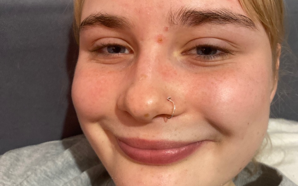 
        Młoda kobieta z kolczykiem w nosie, uśmiechająca się do obiektywu.
    