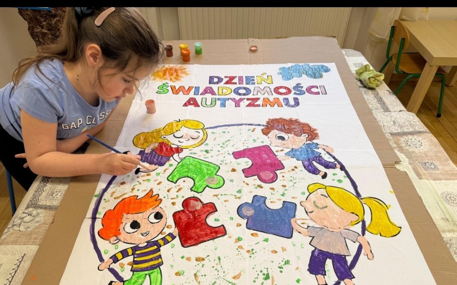 
        Dziewczynka malująca plakat z okazji Dnia Świadomości Autyzmu.
    