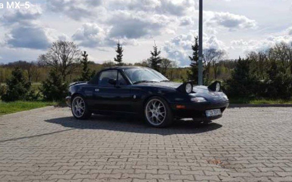 
        Czarny samochód sportowy na parkingu, w otoczeniu natury.
    