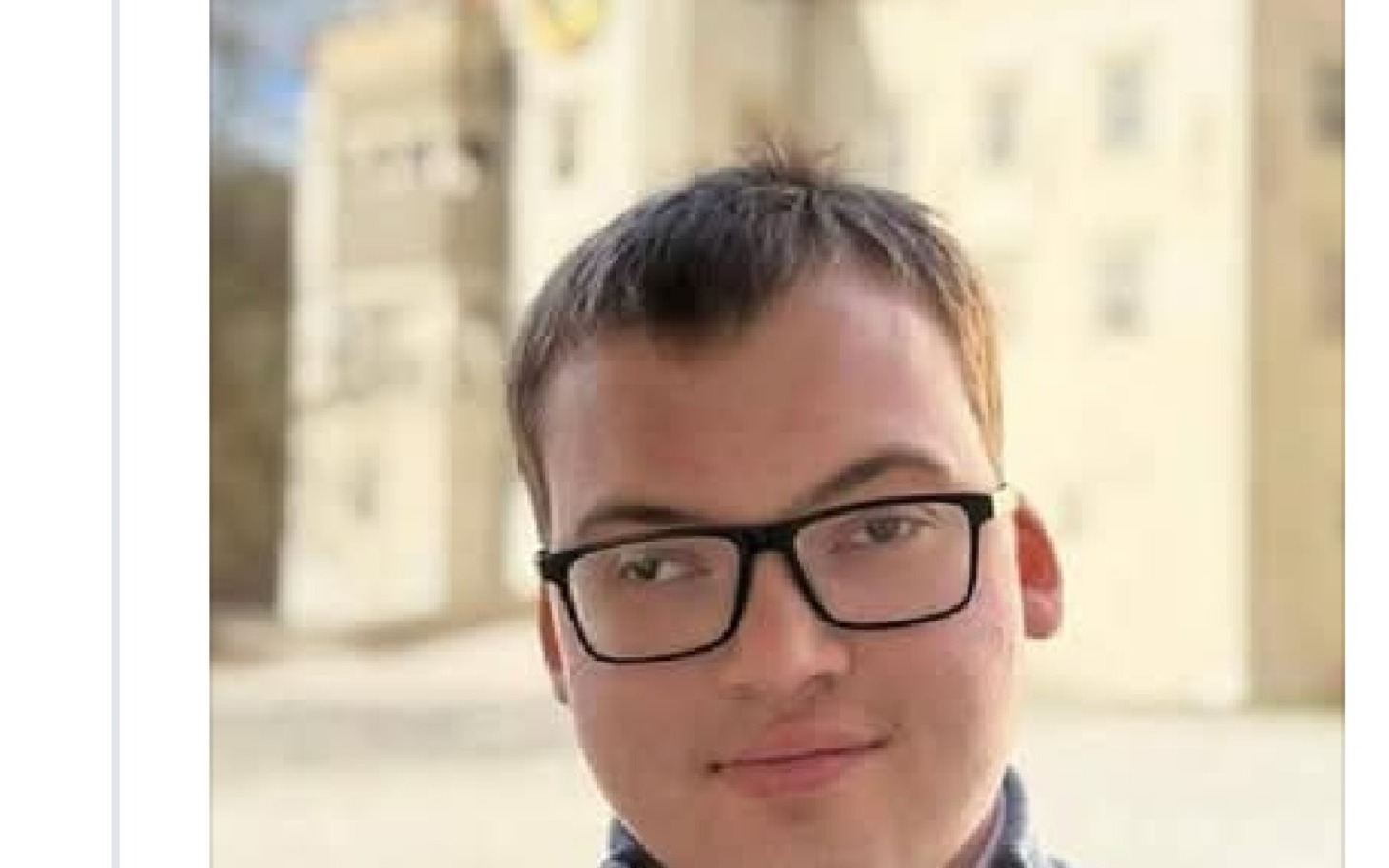 
        Młody mężczyzna w okularach na tle budynku.
    