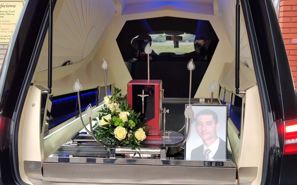 Wnętrze karawanu z kwiatami i zdjęciem zmarłego.