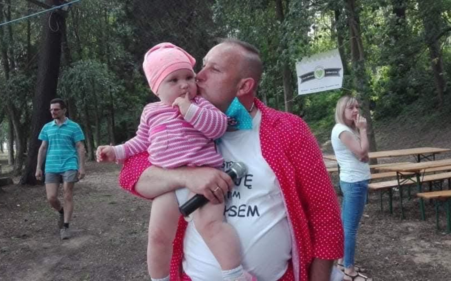 
        Mężczyzna z dzieckiem na rękach w parku.
    