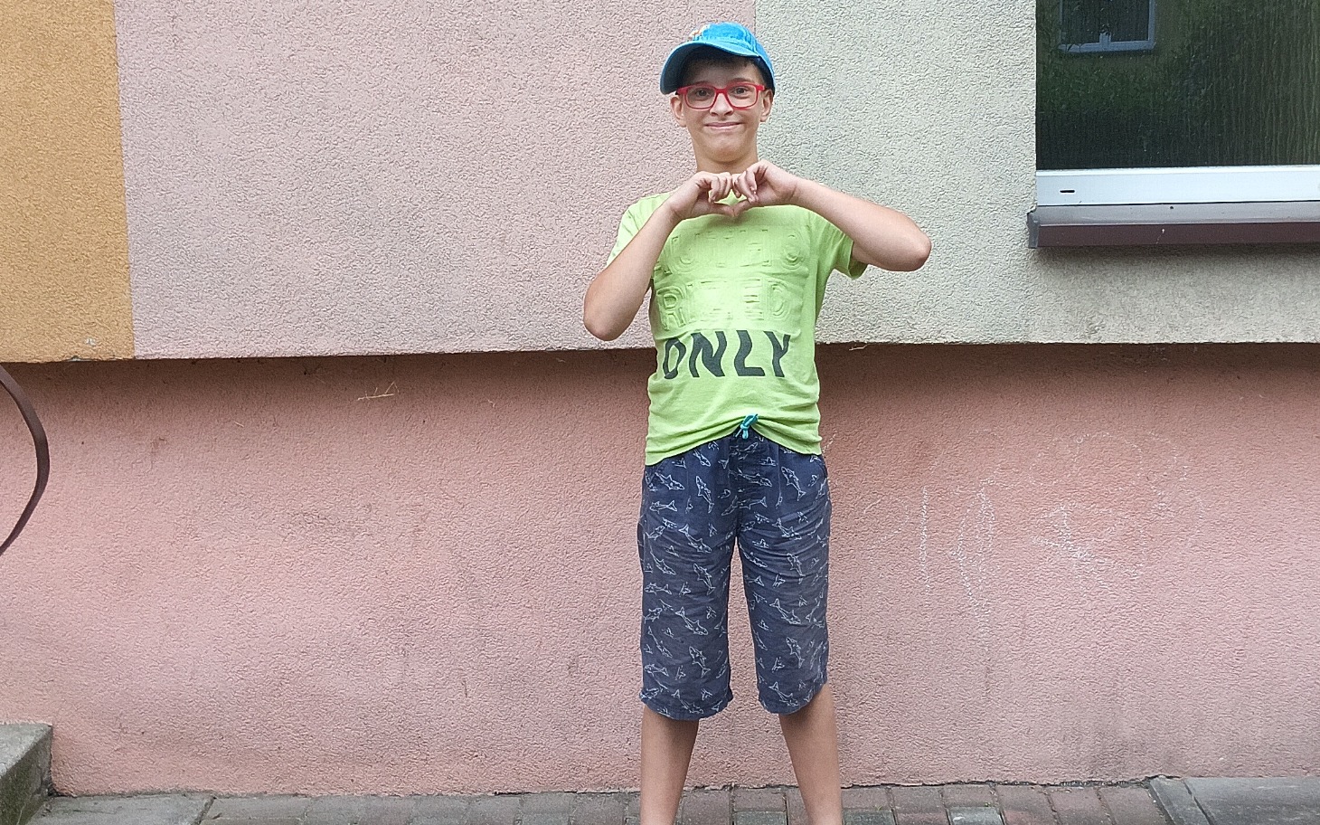 
        Chłopiec w kolorowej koszulce, pozujący na tle ściany.
    