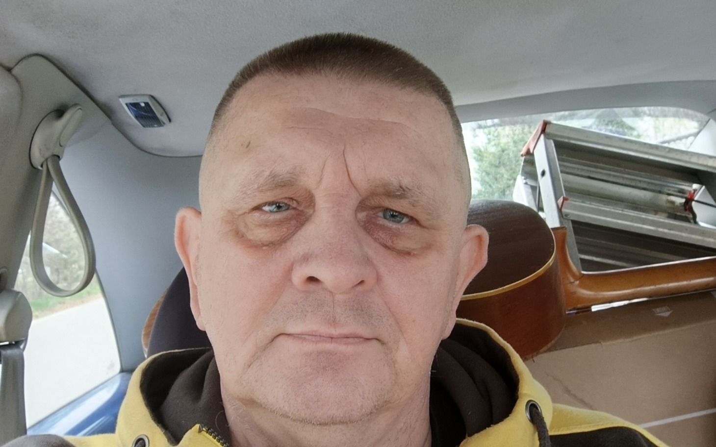 
        Mężczyzna w samochodzie, z gitarą w tle.
    