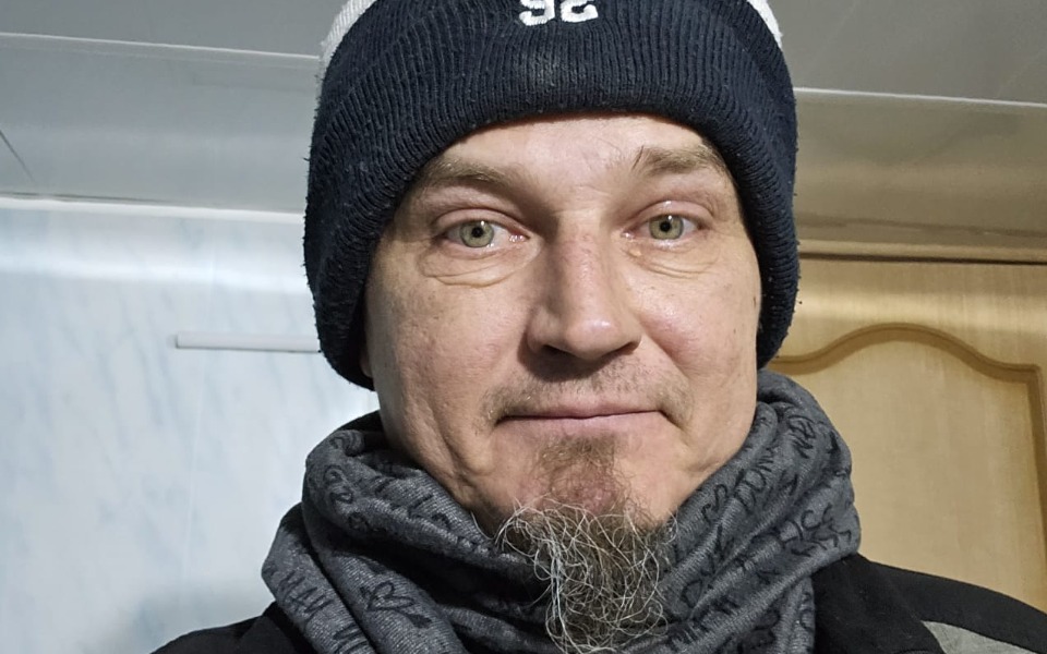 Mężczyzna w czapce i szaliku, uśmiechający się do kamery.