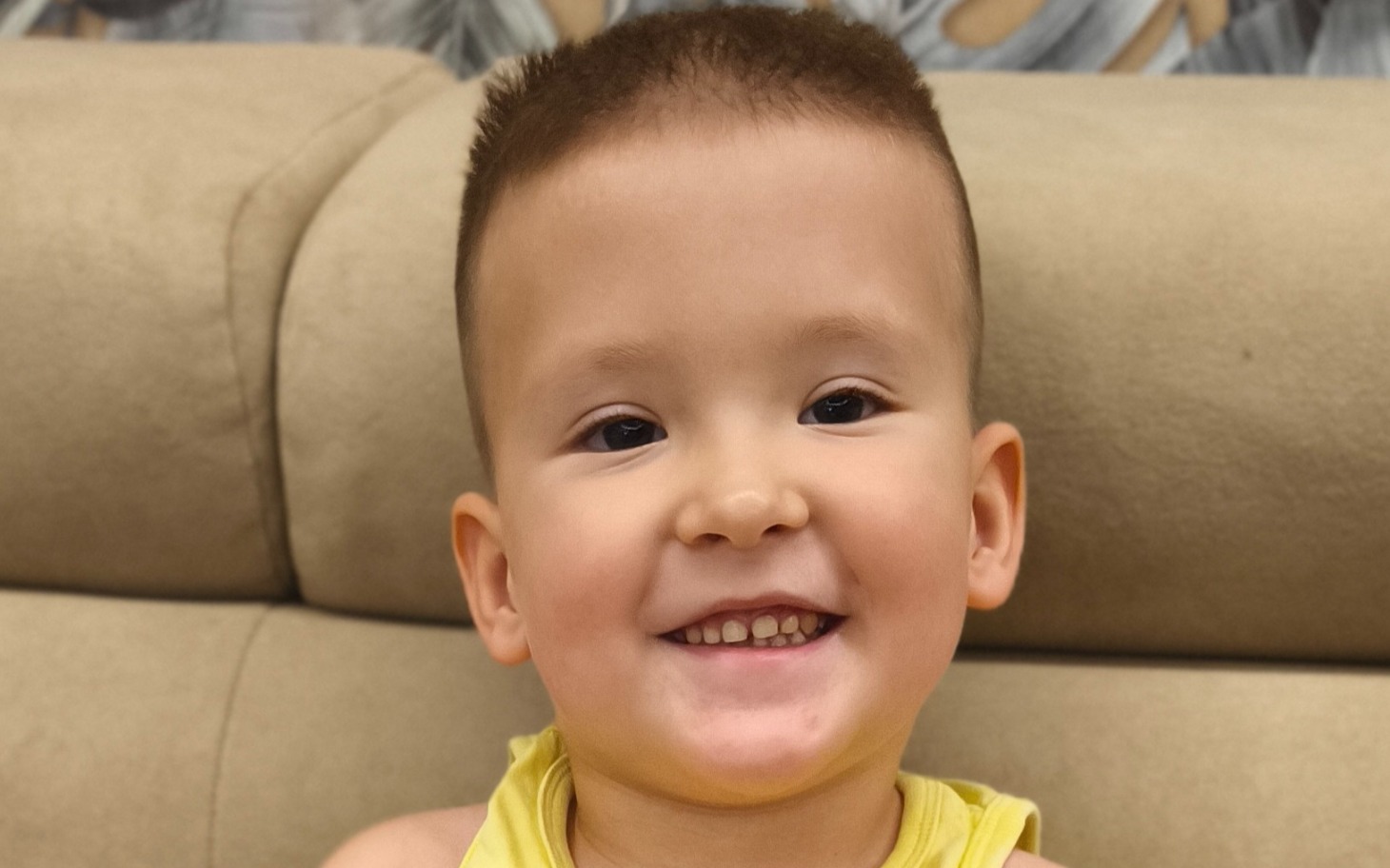 
        Uśmiechnięty chłopiec w żółtej koszulce na tle kanapy.
    