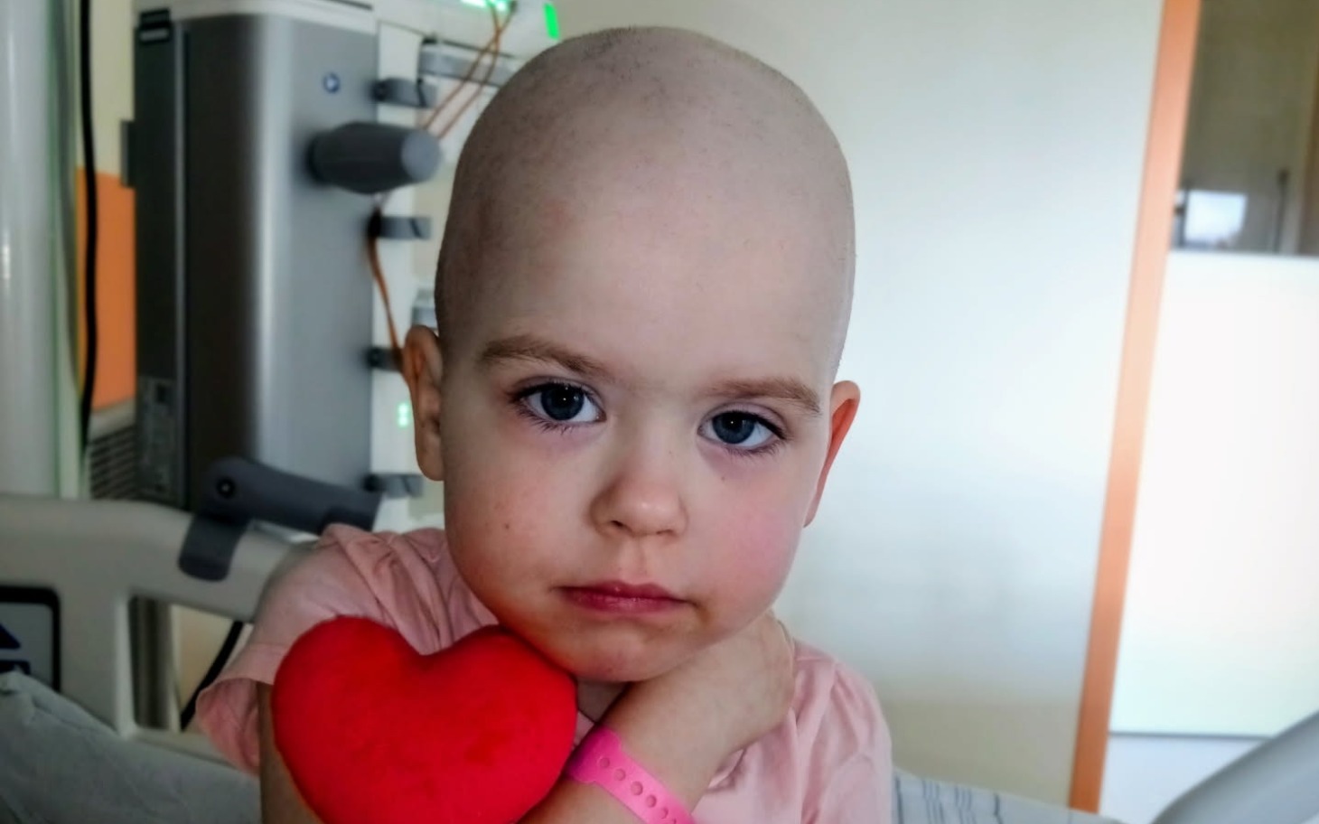 Mała dziewczynka z sercem w rękach, w szpitalnym łóżku.