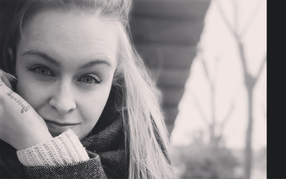 
        Kobieta z uśmiechem, trzymająca rękę przy twarzy.
    