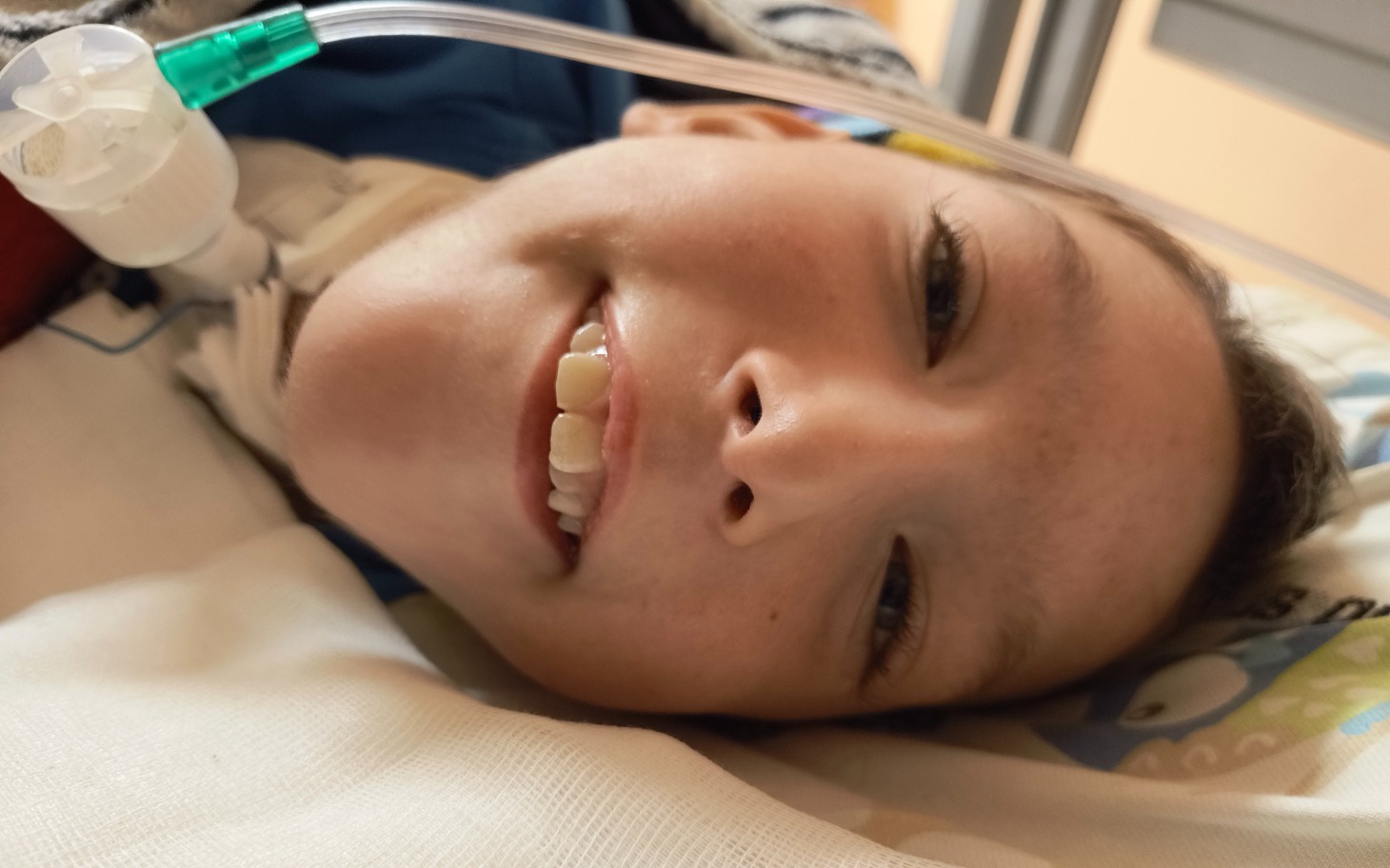 
        Chłopiec uśmiechający się, leżący w szpitalnym łóżku.
    