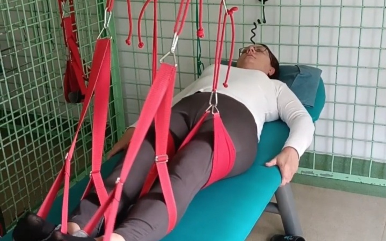 
        Kobieta leżąca na stole terapeutycznym, używająca sprzętu rehabilitacyjnego.
    