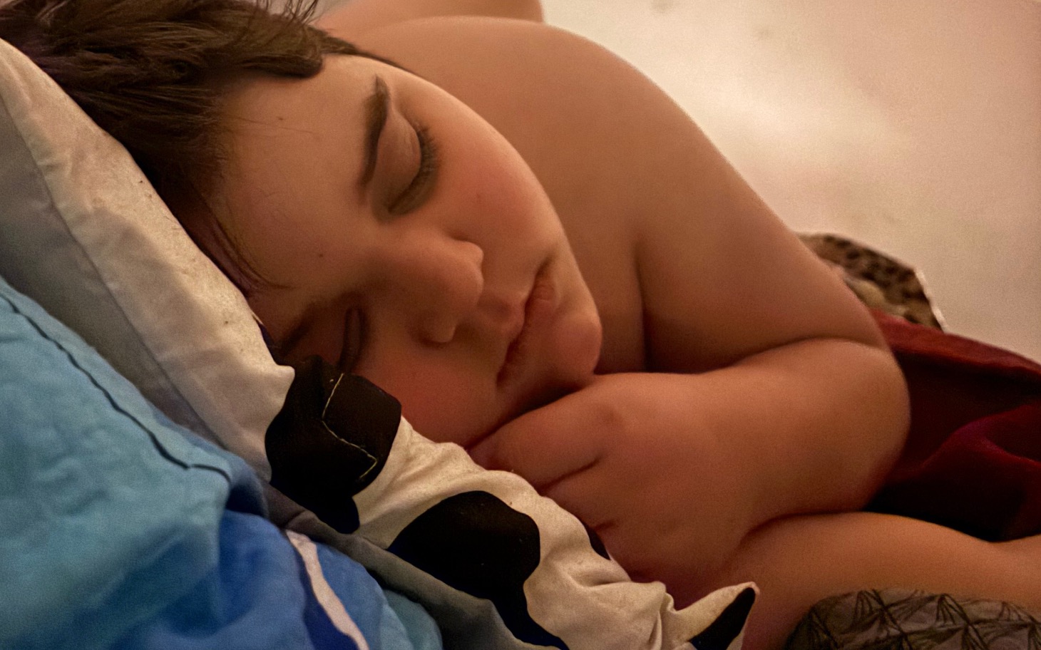 
        Chłopiec śpi spokojnie na łóżku, otulony kołdrą.
    