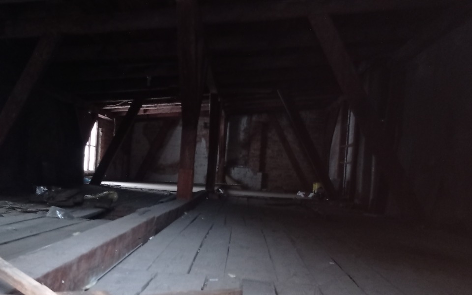 
        Ciemne wnętrze strychu z drewnianymi belkami.
    