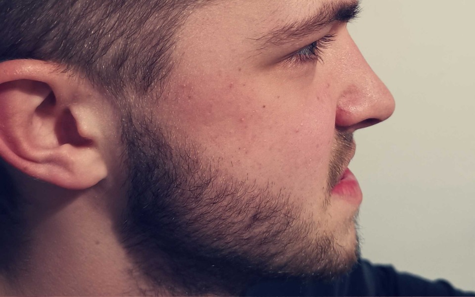 
        Profil mężczyzny z zarostem, skupiony na czymś.
    