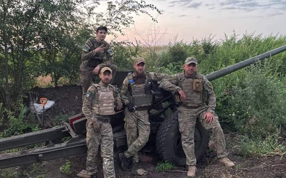 
        Czterech żołnierzy w mundurach przy działa, w otoczeniu zieleni.
    