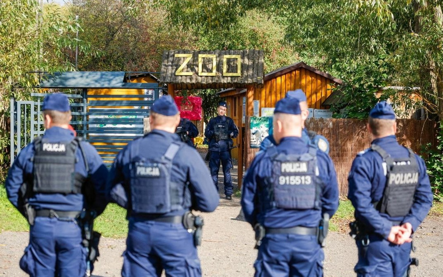 
        Wjazd do ogrodu zoologicznego z napisem ZOO i grupą policjantów na drodze.
    