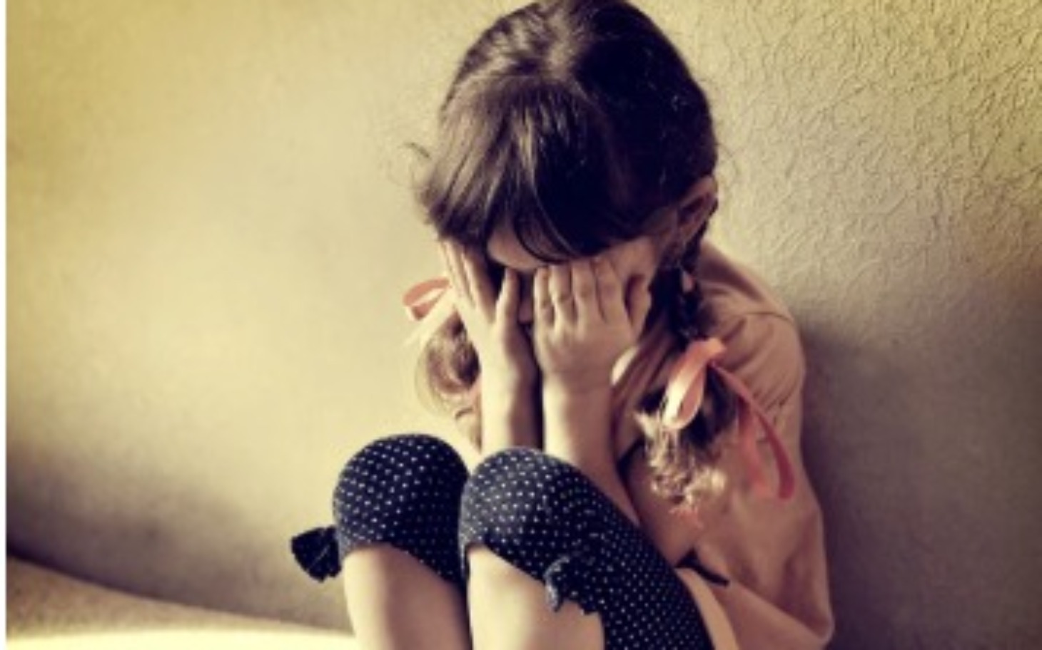 
        Dziewczynka z zasłoniętą twarzą, wyrażająca smutek.
    