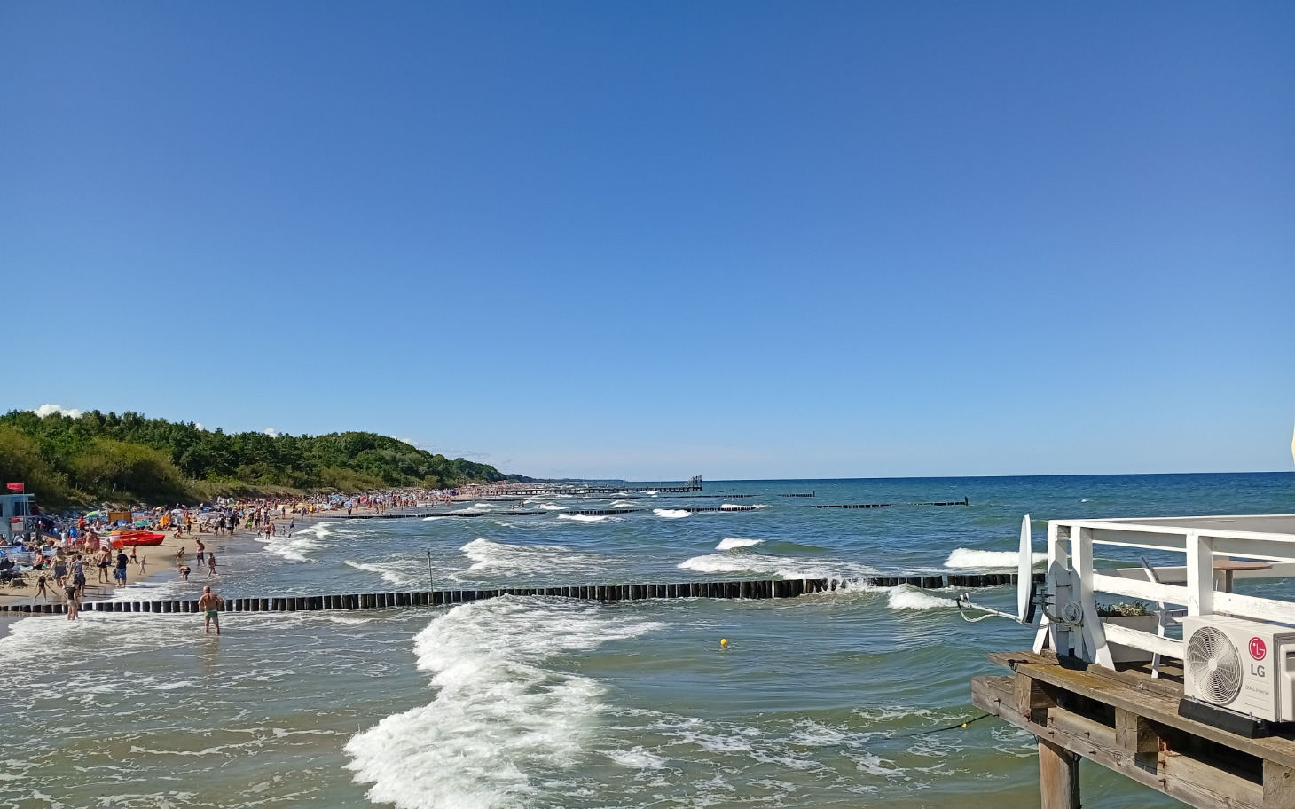 
        Plaża z falami i tłumem ludzi w słoneczny dzień.
    