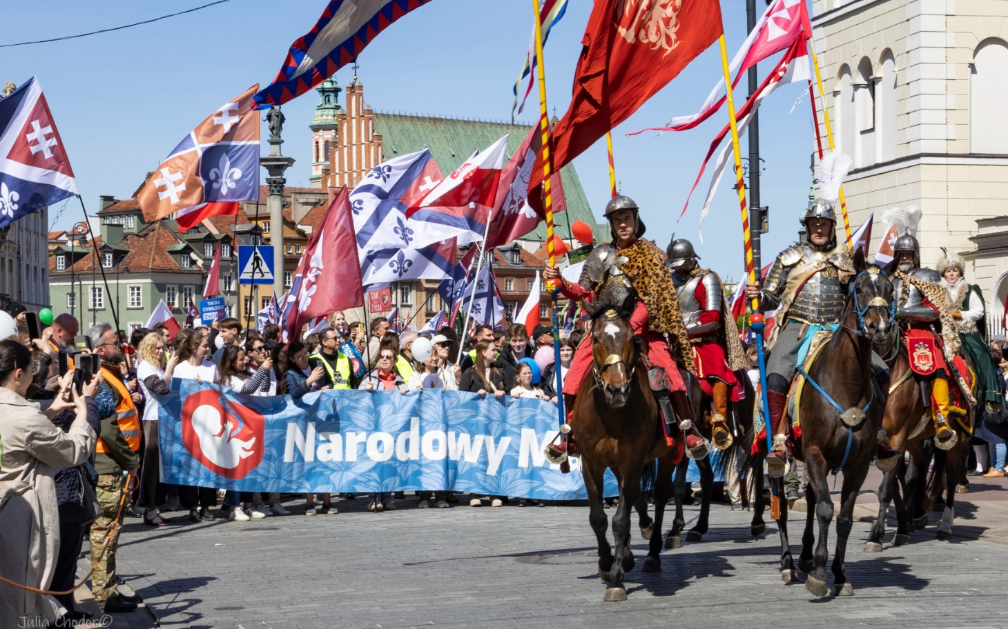 
        Parada z rycerzami na koniach, z flagami i transparentem.
    