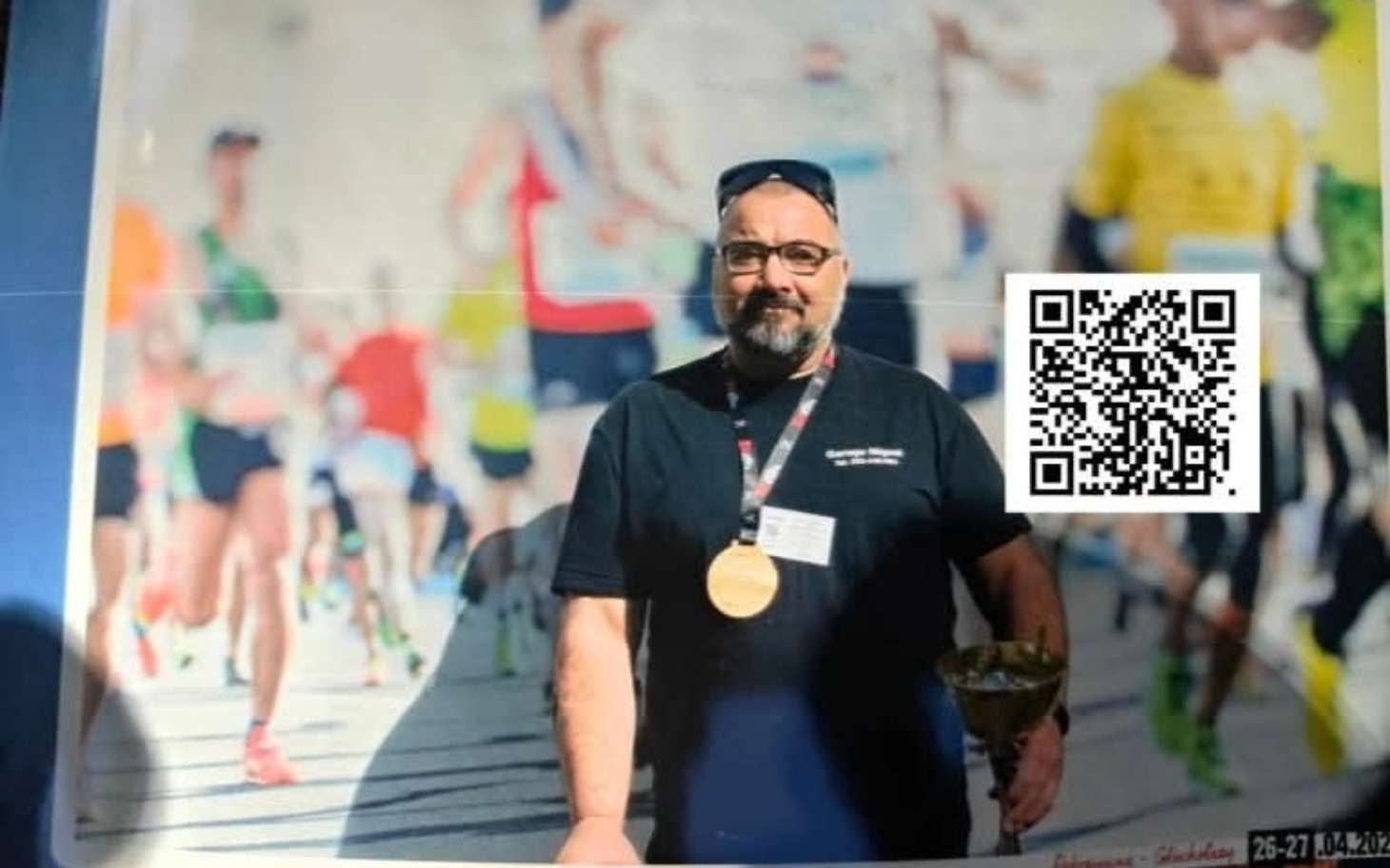 
        Mężczyzna z medalem i pucharem na tle biegaczy.
    