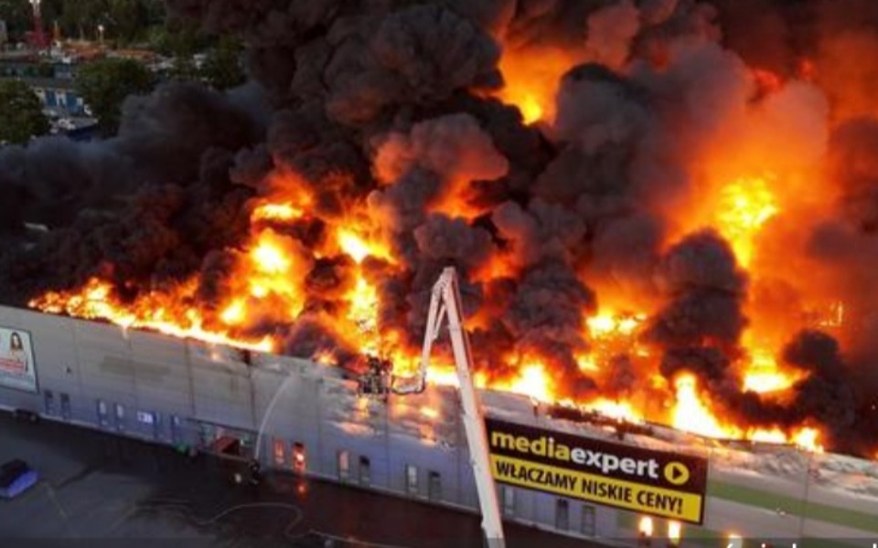 
        Pożar w dużym budynku, intensywne płomienie i dym.
    