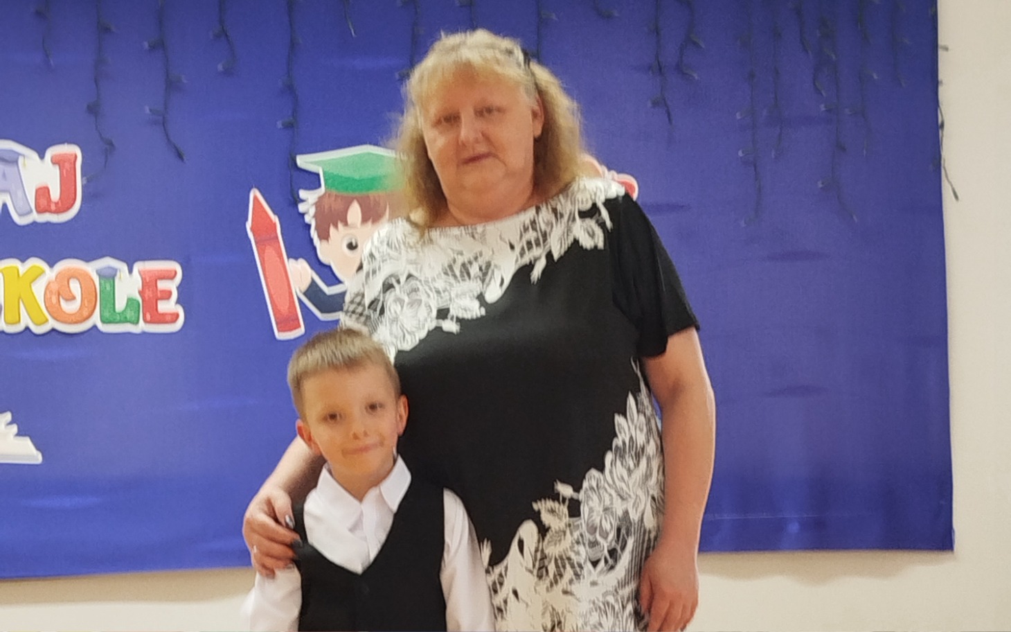 
        Dziecko z dorosłym na tle dekoracji szkolnej, chwila radości.
    