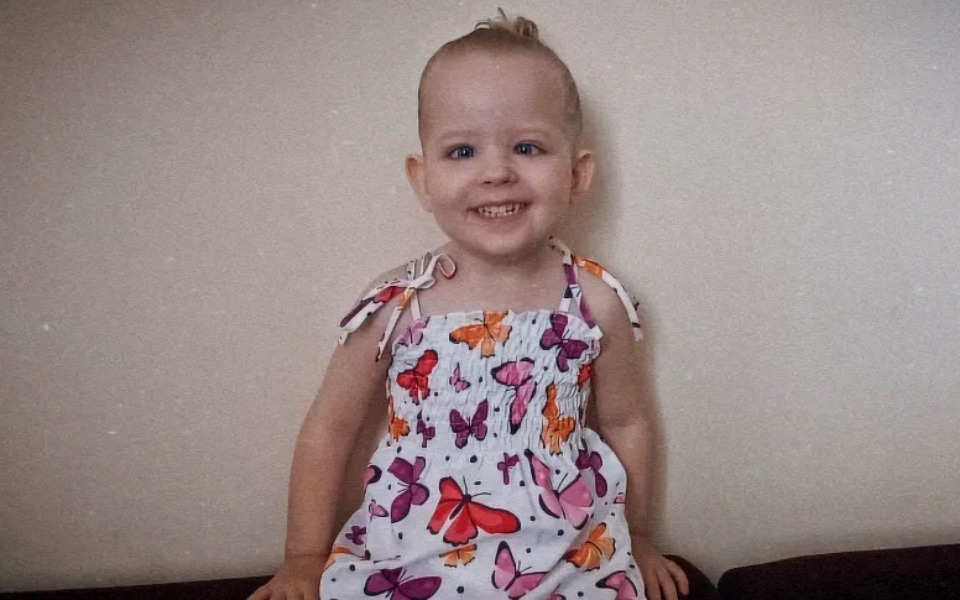 
        Mała dziewczynka w kolorowej sukience, uśmiechająca się do kamery.
    