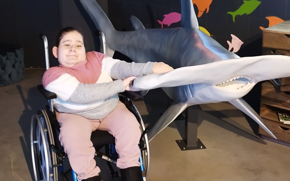 Dziecko na wózku inwalidzkim, trzymające rekina z plastiku.