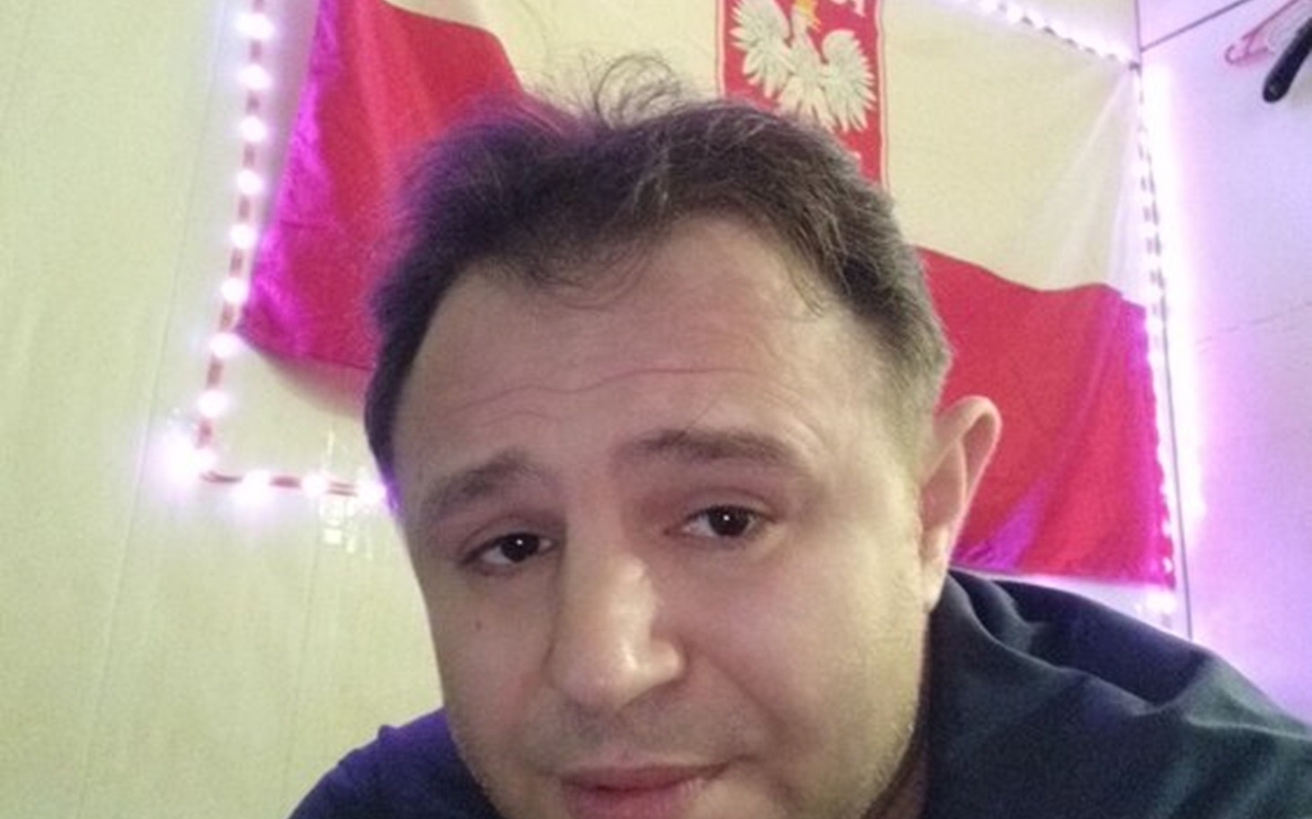 
        Mężczyzna z flagą Polski w tle, uśmiechający się do kamery.
    