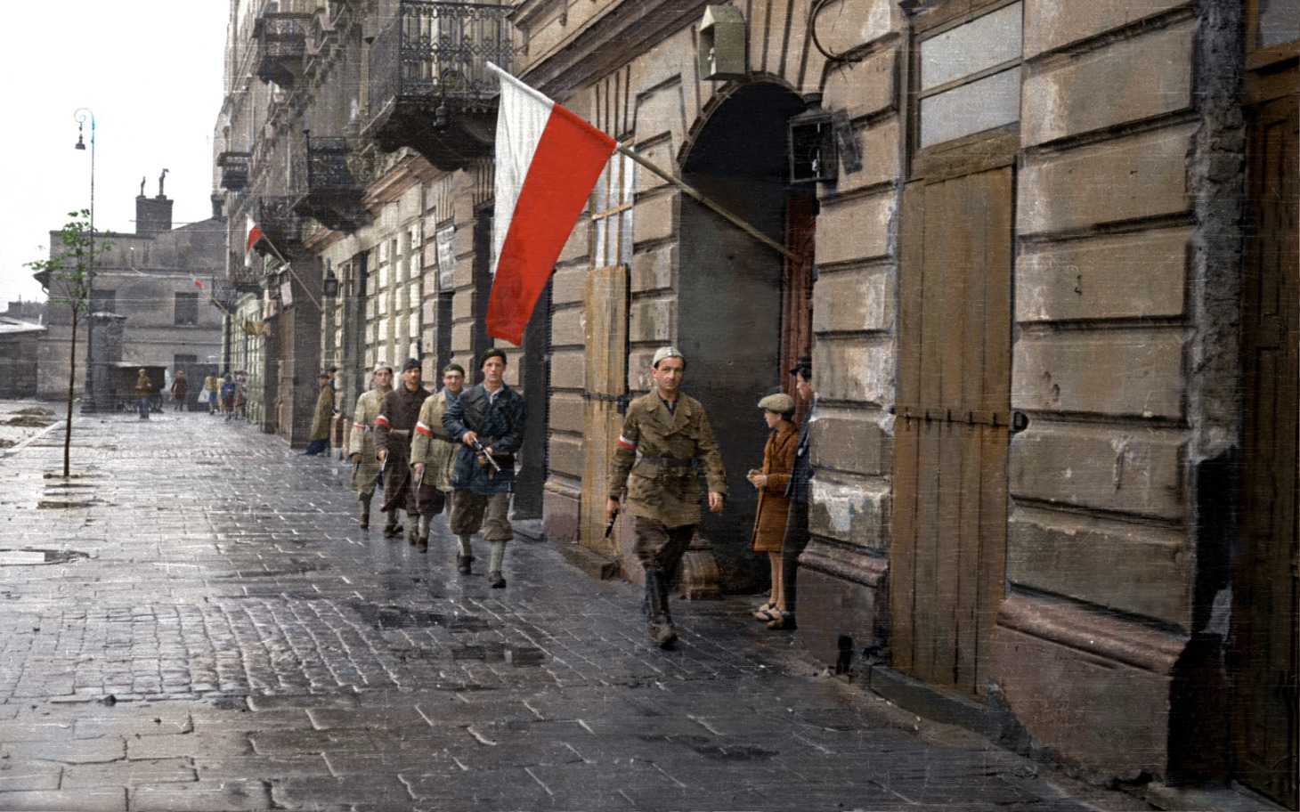
        Grupa żołnierzy idących ulicą z flagami Polski.
    