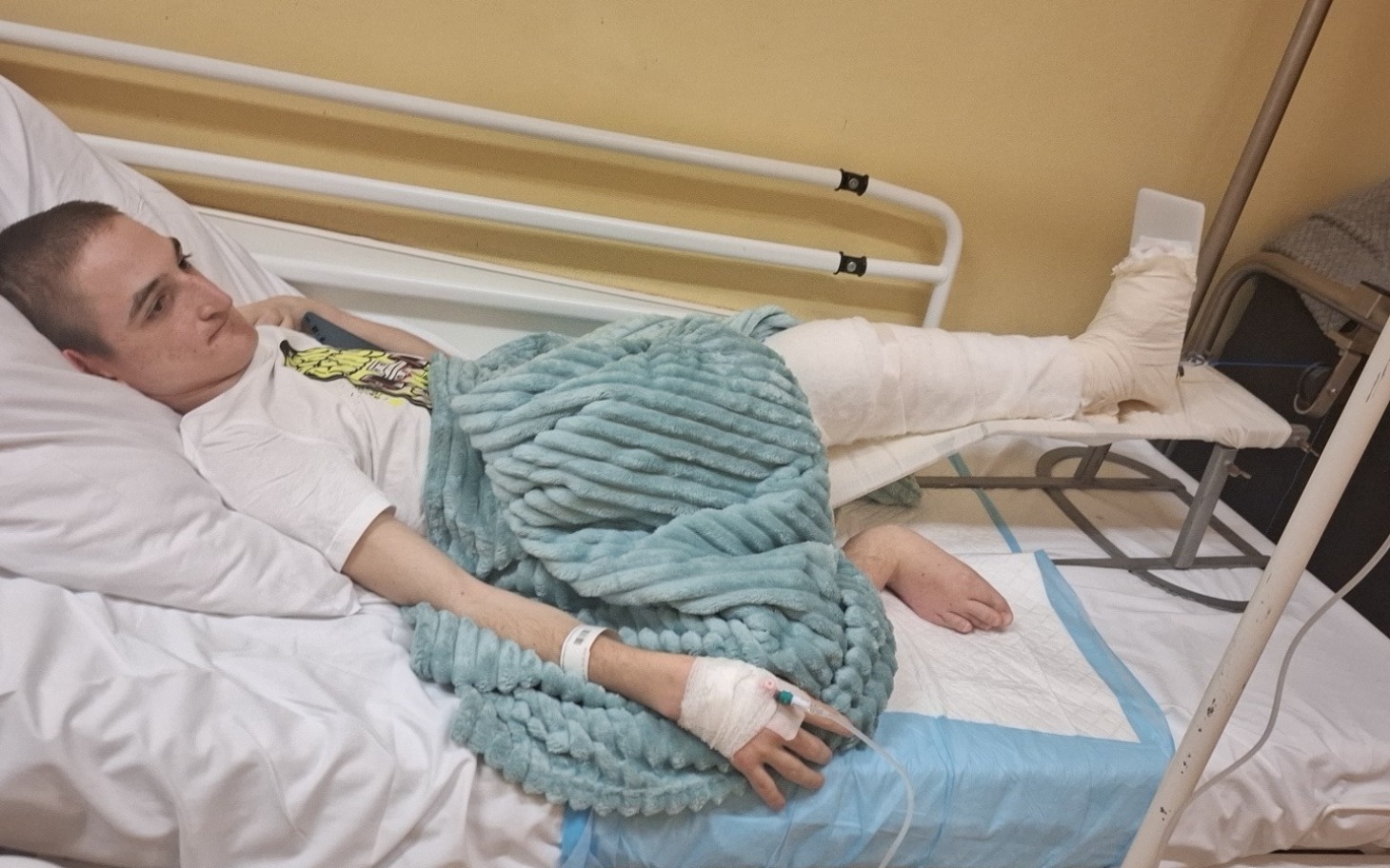 
        Młody chłopak leżący w szpitalnym łóżku z opatrunkami.
    