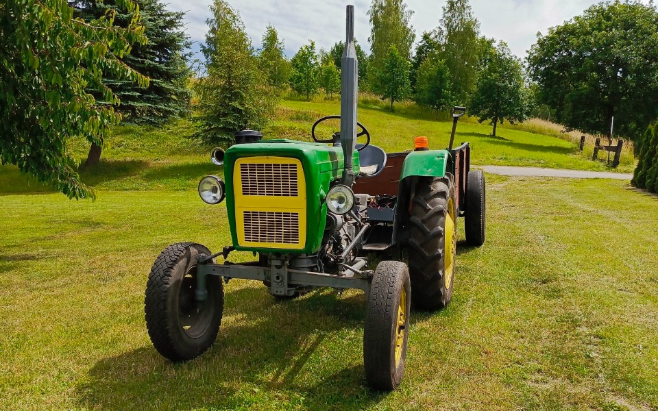 
        Traktor na zielonej łące, otoczony drzewami.
    