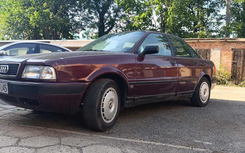 
        Czerwony samochód zaparkowany na podjeździe, otoczony zielenią.
    