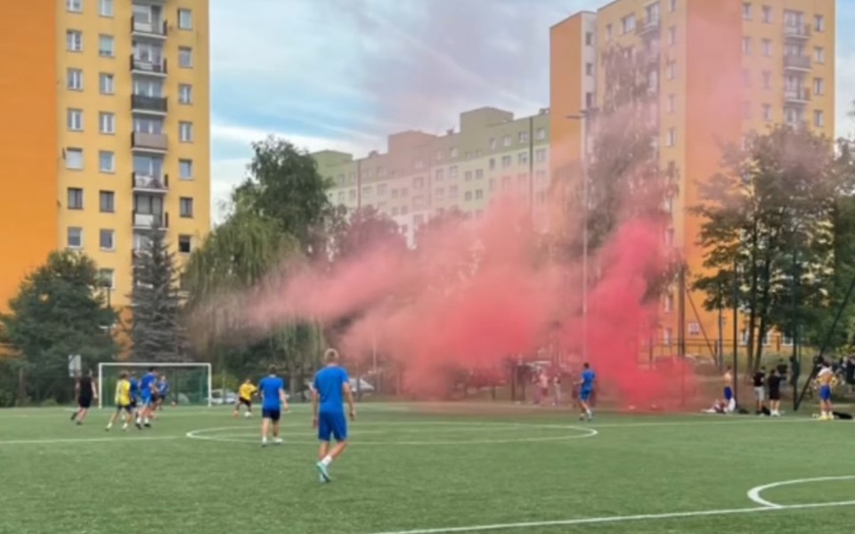
        Mecz piłkarski z dymem w tle, zawodnicy w niebieskich strojach.
    