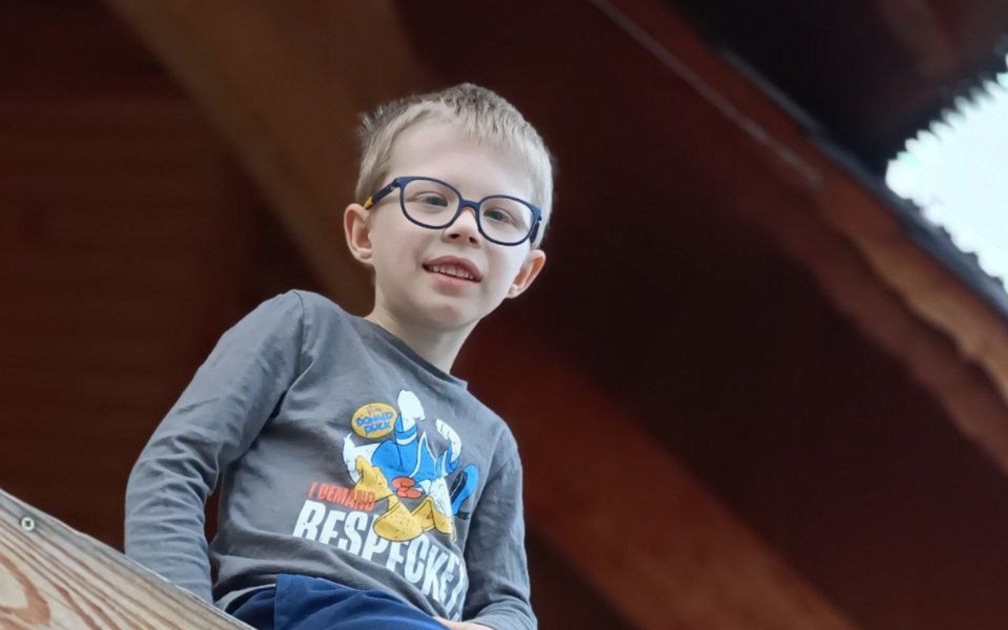 
        Chłopiec w okularach uśmiechający się z wysokości.
    