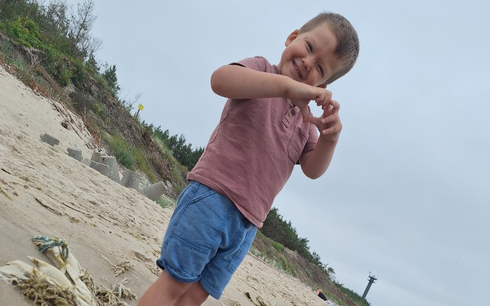 
        Chłopiec na plaży, robiący serce z rąk.
    