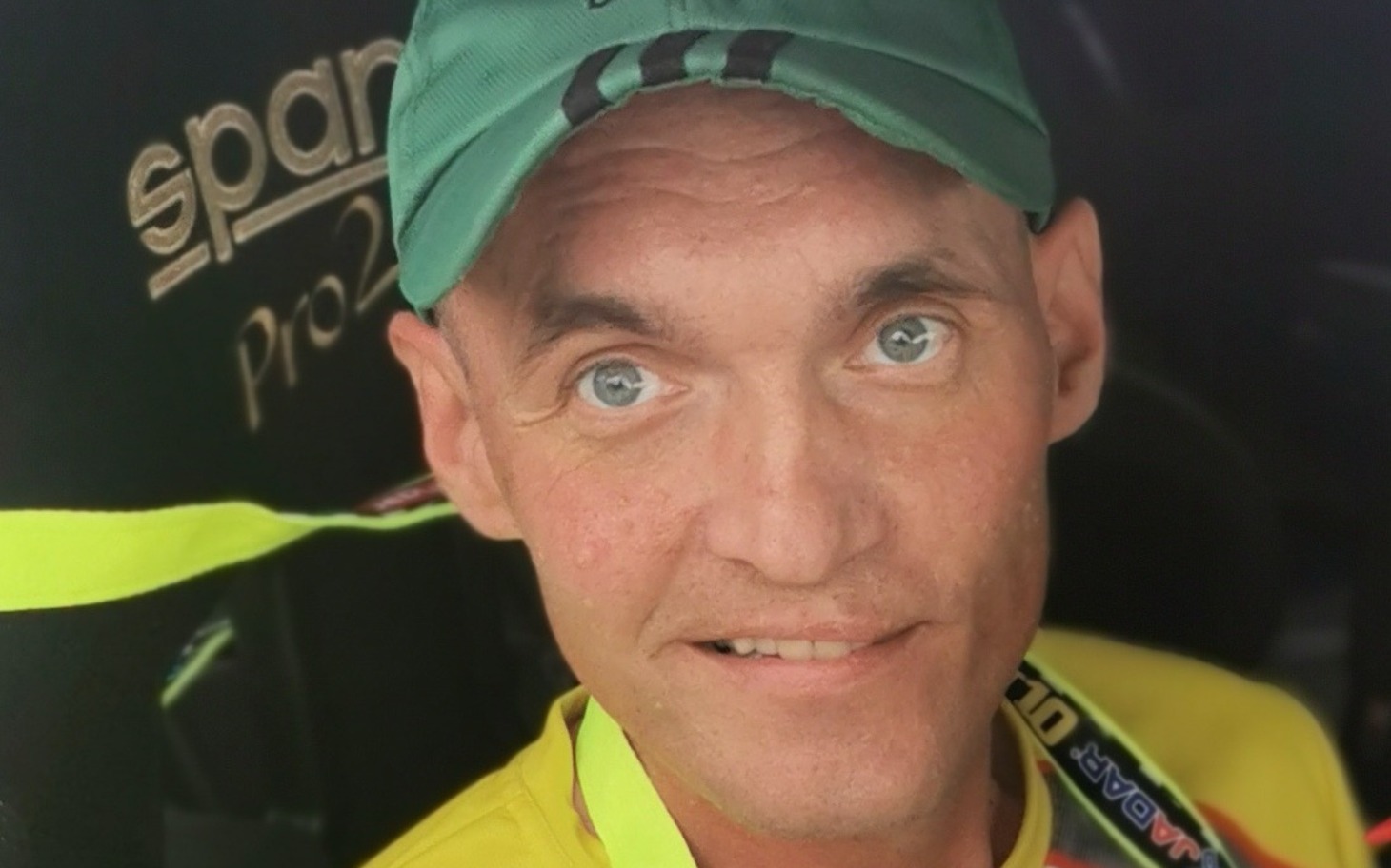 
        Mężczyzna w czapce, uśmiechający się w samochodzie wyścigowym.
    