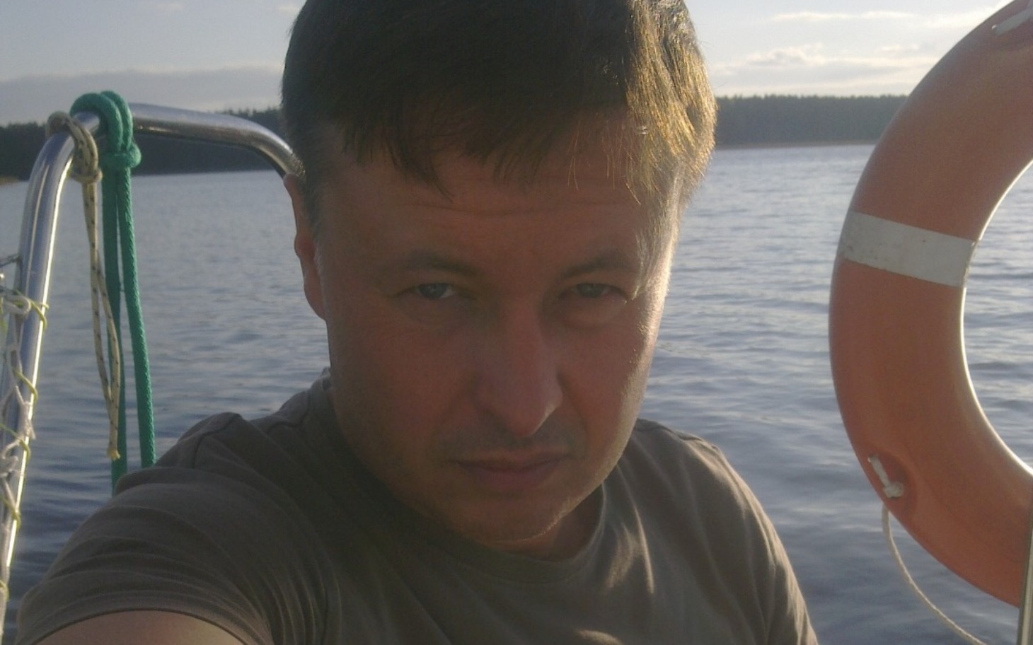 Mężczyzna na łodzi, patrzący w stronę kamery, w tle woda.