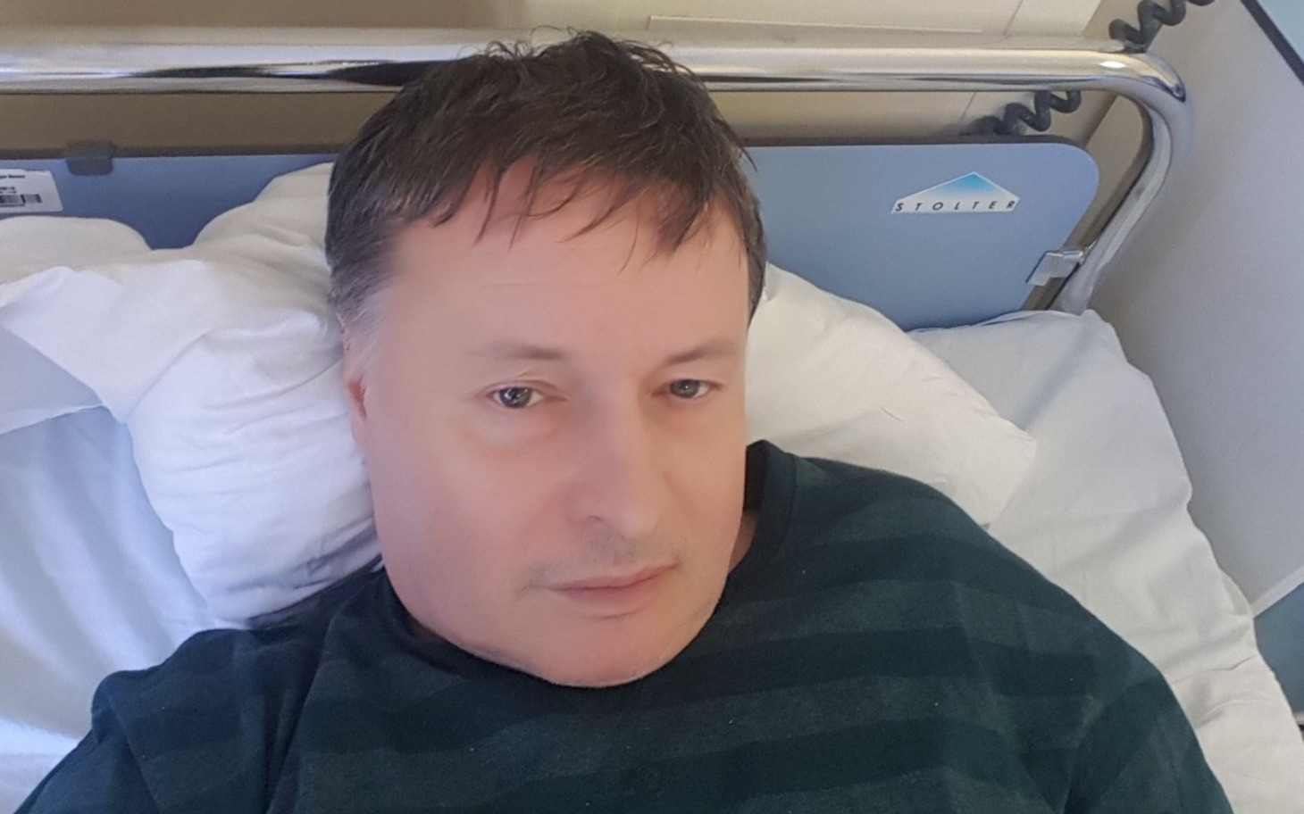 
        Mężczyzna leży na łóżku w szpitalnym pokoju, odpoczywający
    