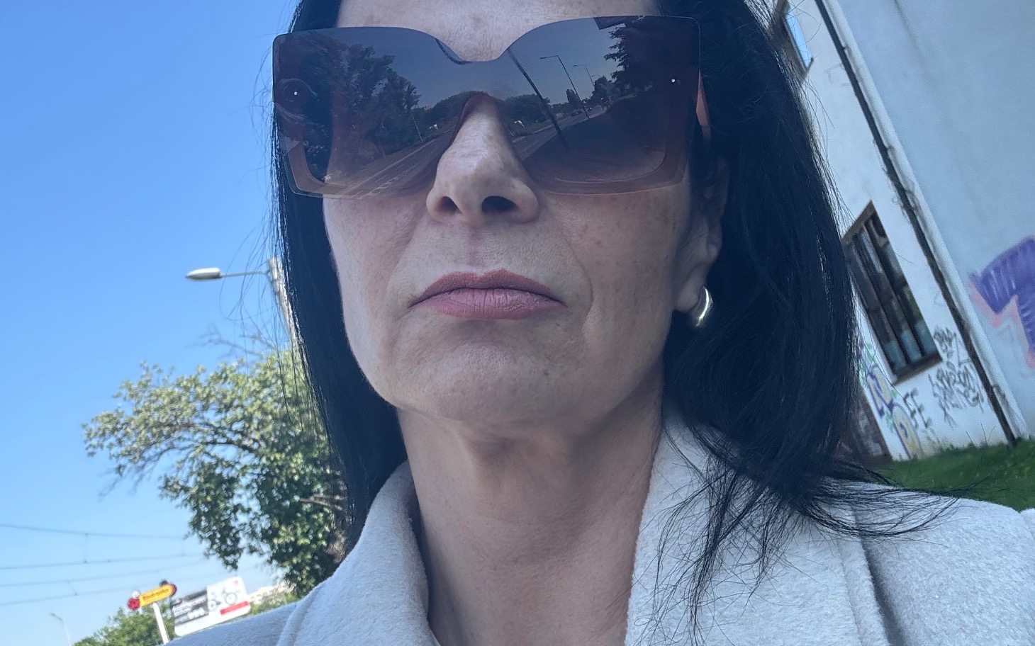 
        Kobieta w okularach przeciwsłonecznych na tle nieba i ulicy.
    