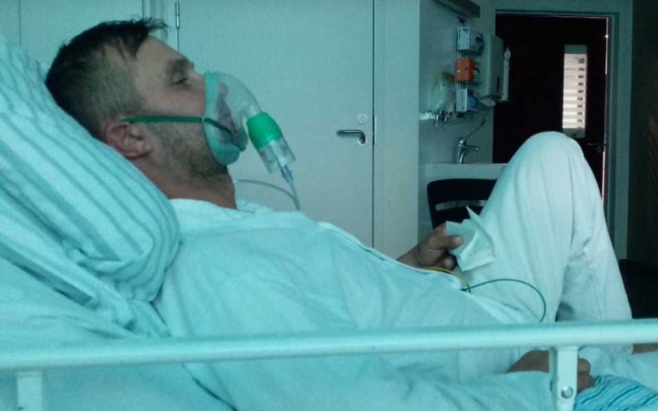 
        Mężczyzna w szpitalu z maską tlenową, leżący na łóżku szpitalnym.
    