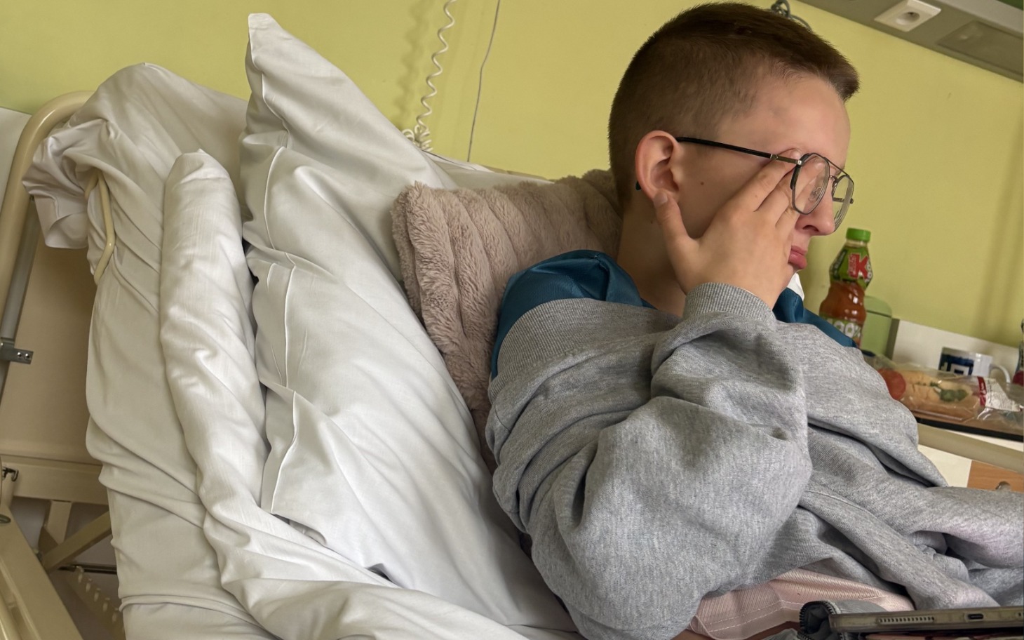 
        Chłopiec w szpitalnym łóżku, z wyrazem zmęczenia na twarzy.
    