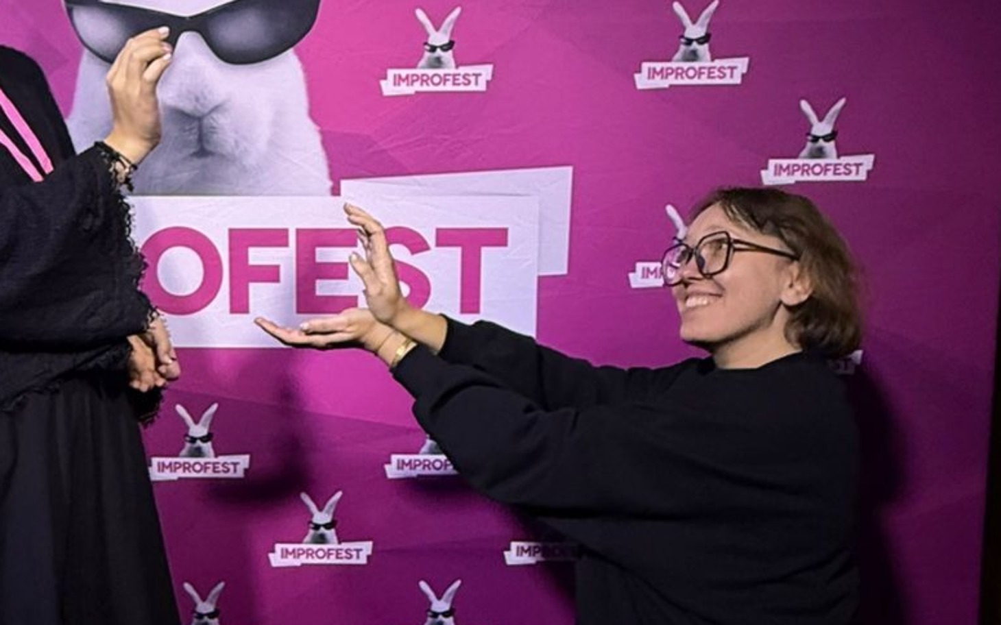 
        Osoba pozująca na tle kolorowego tła z napisem IMPROFEST.
    