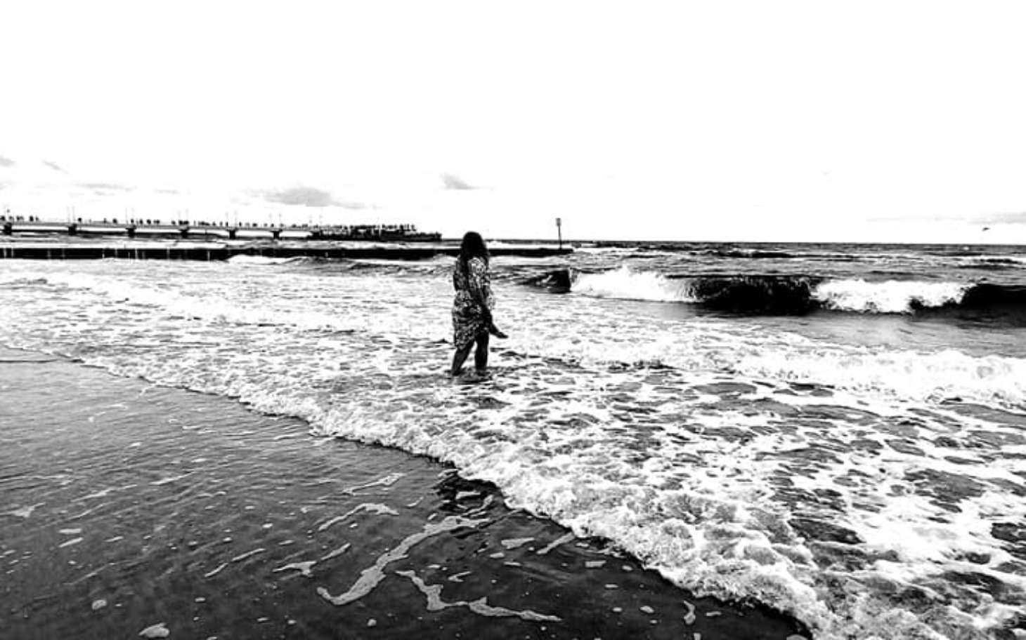 
        Kobieta spacerująca po plaży, fale uderzają w brzeg.
    