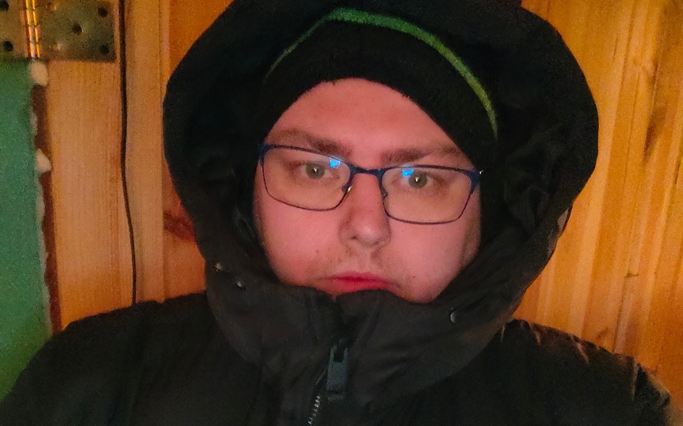 
        Mężczyzna w ciepłej kurtce, z kapturem, w zimowej scenerii.
    