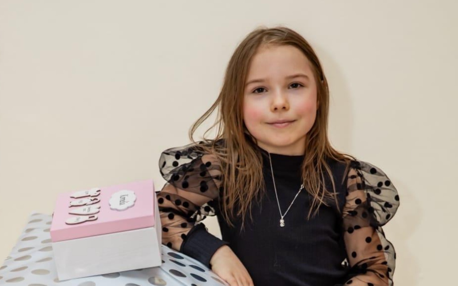 
        Młoda dziewczynka pozująca z prezentem na stole.
    