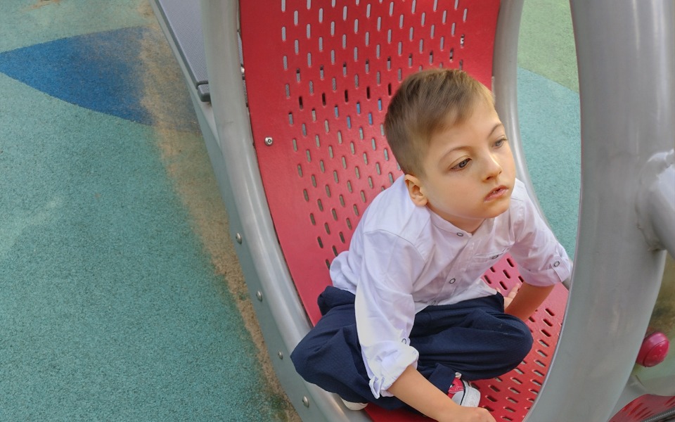 
        Chłopiec siedzący na huśtawce, zamyślony i smutny.
    